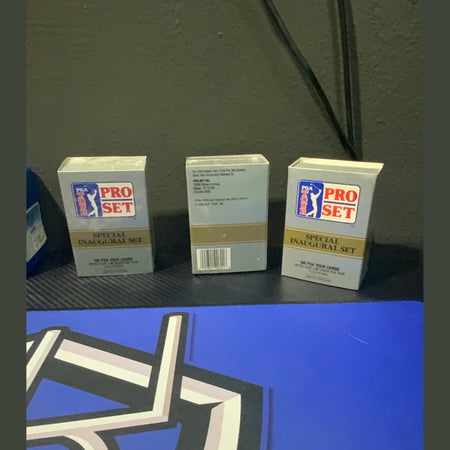 Three Pro Set trading card packs on a dark surface with a blue background featuring a logo.