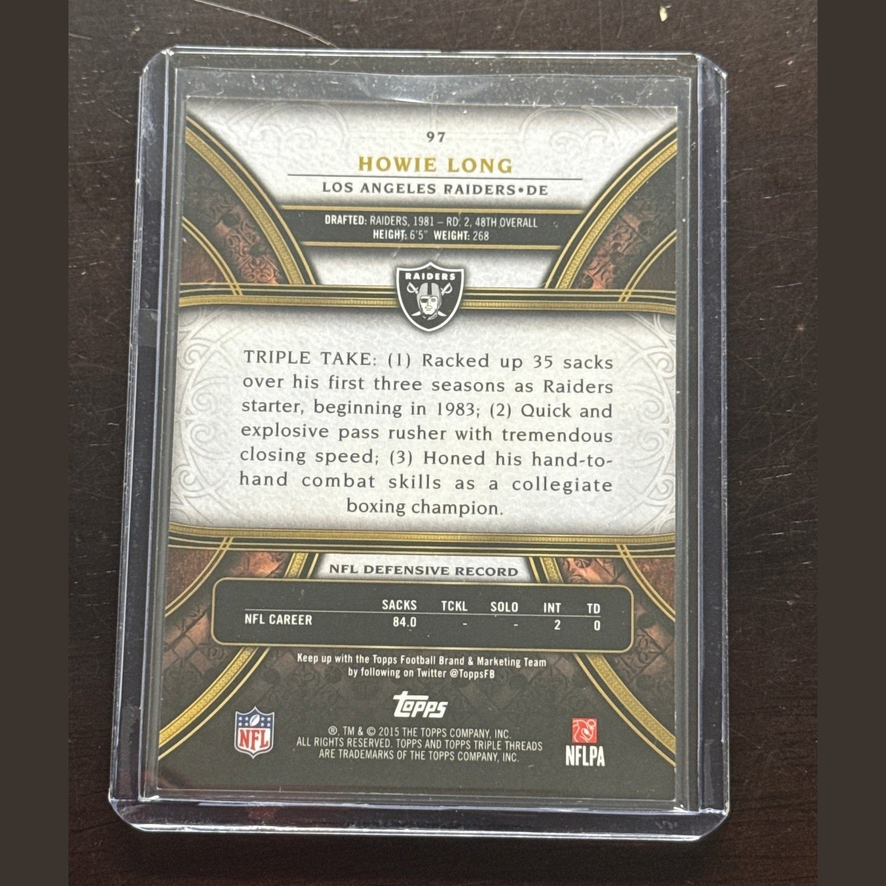 Trading card of Howie Long in a clear protective case on a dark surface