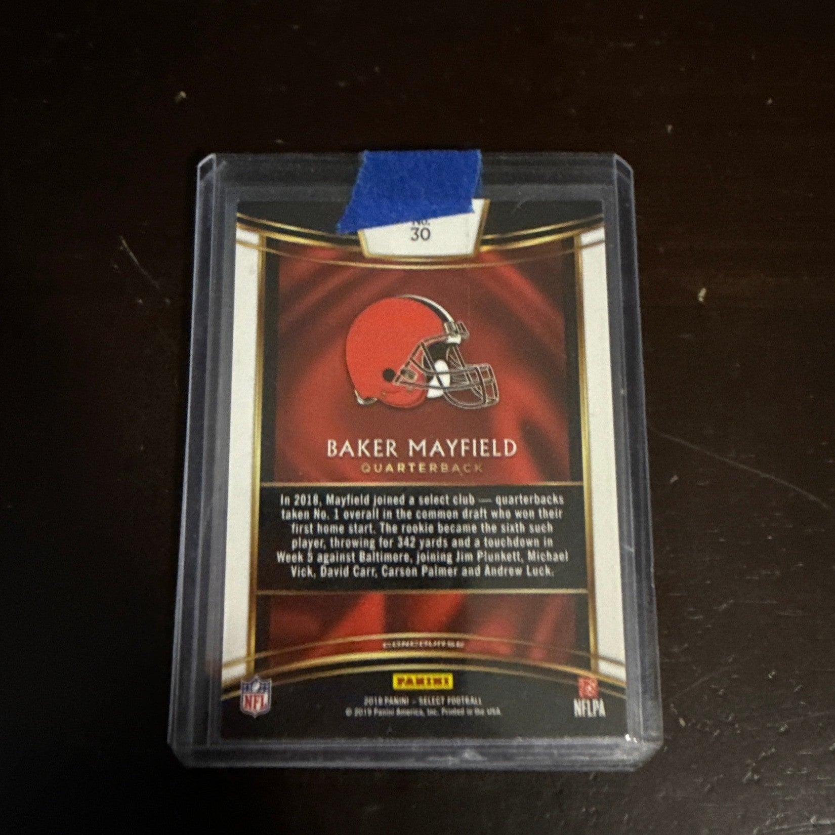 Trading card of Baker Mayfield in a clear protective case on a dark surface