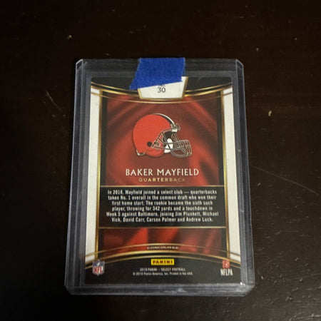 Trading card of Baker Mayfield in a clear protective case on a dark surface