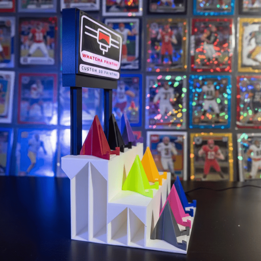 Colorful 3D printed objects on a stand with a 3D printer in the background.