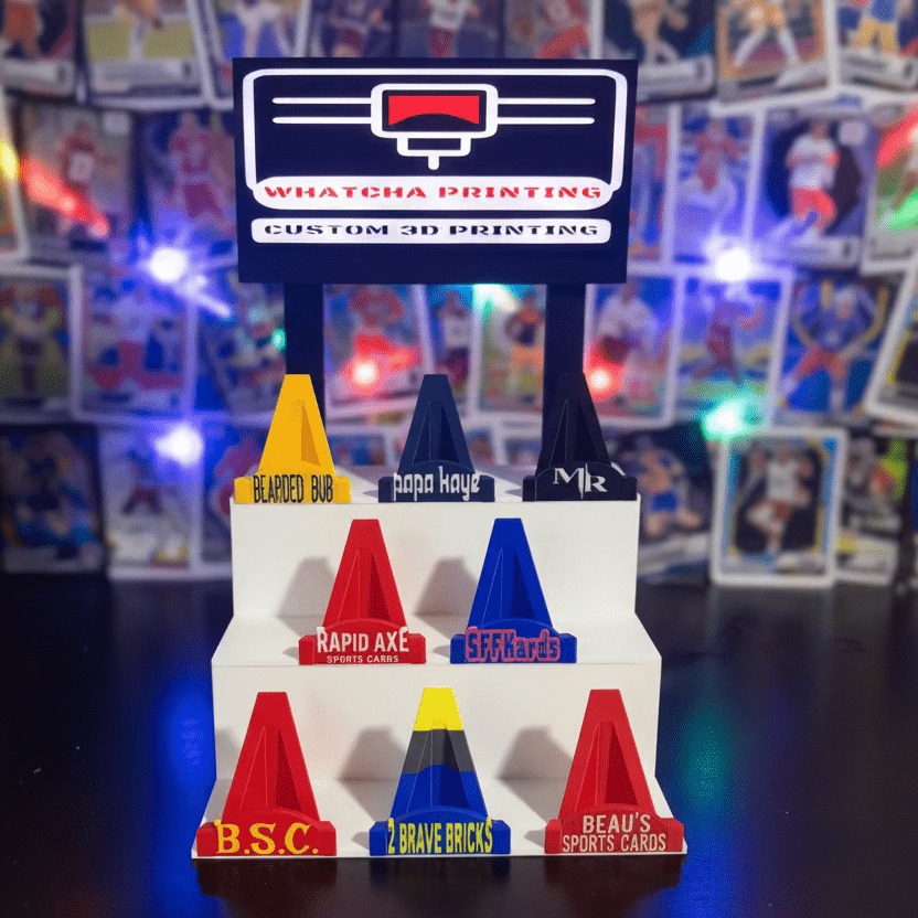 Colorful 3D-printed traffic cone models with branding in front of a 3D printer.