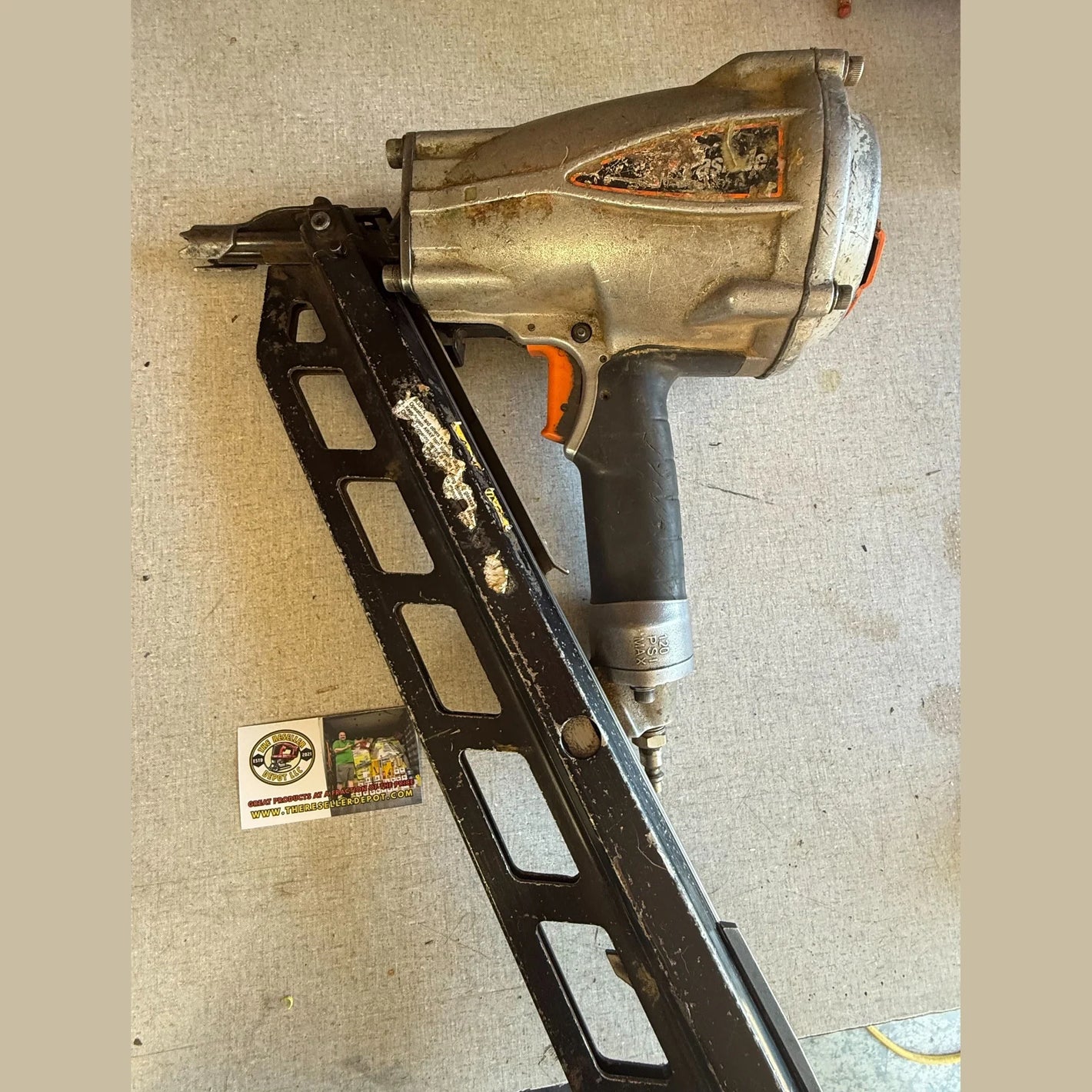 Nail gun on a textured surface with a small box labeled 'Banks' in the background.