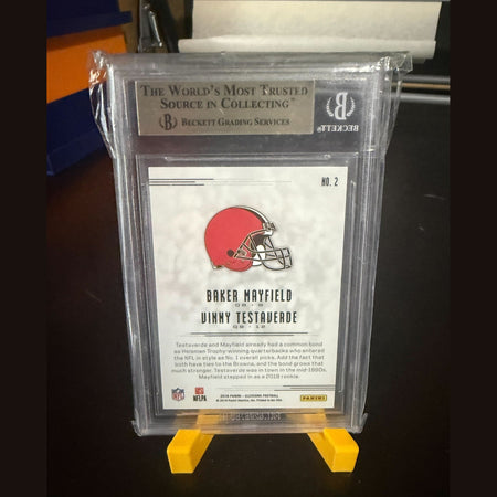 Football trading card in a protective case with a yellow stand on a dark surface
