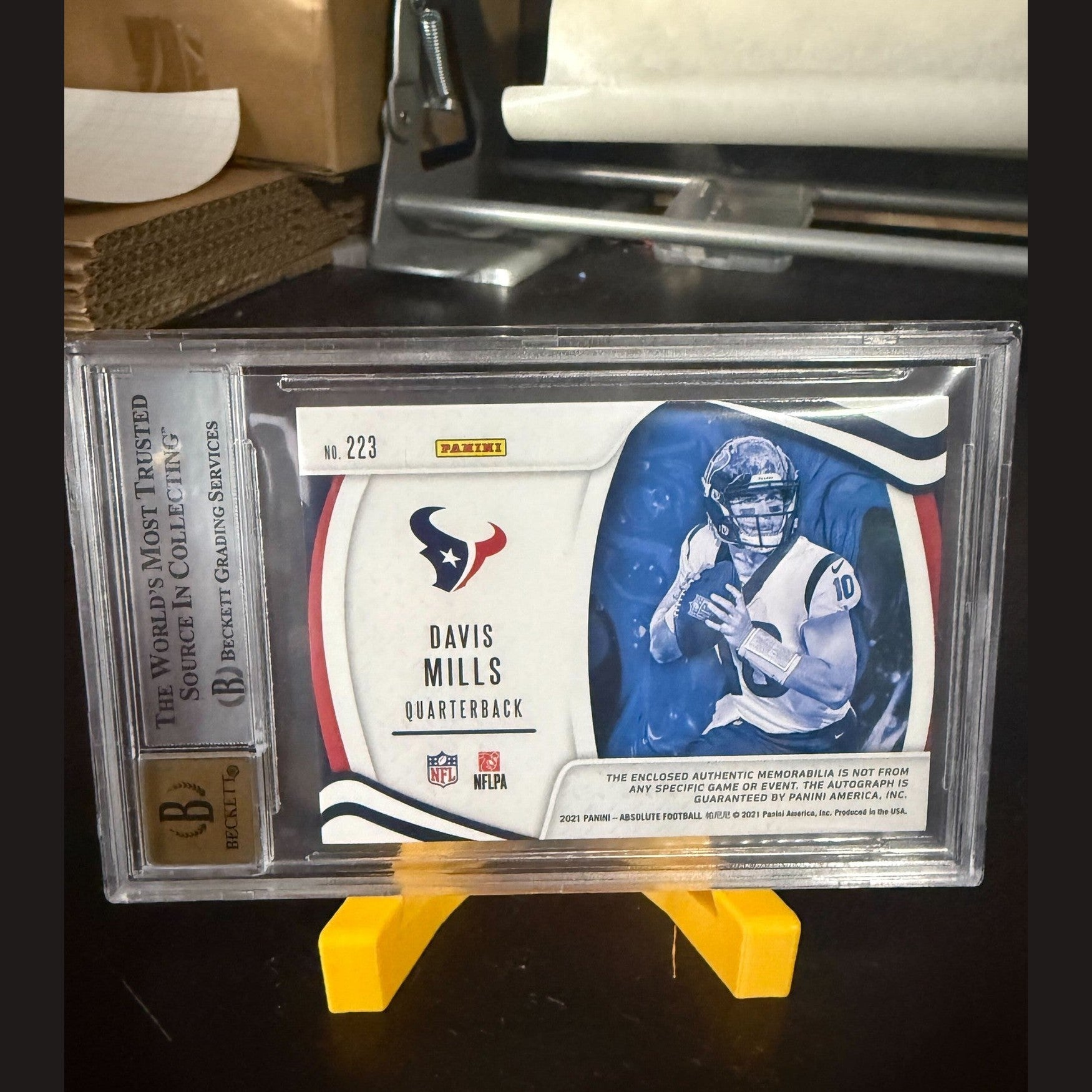 Trading card of a football player in a display case with a yellow stand.