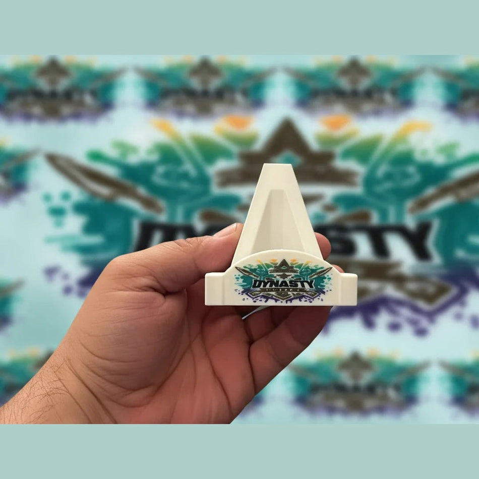 Hand holding a small white object with 'Dynasty' branding in an indoor setting.