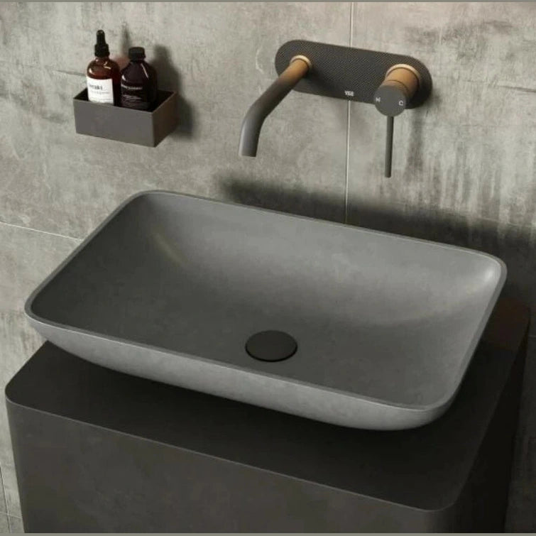 Gray rectangular sink with black faucet against a gray tiled wall.