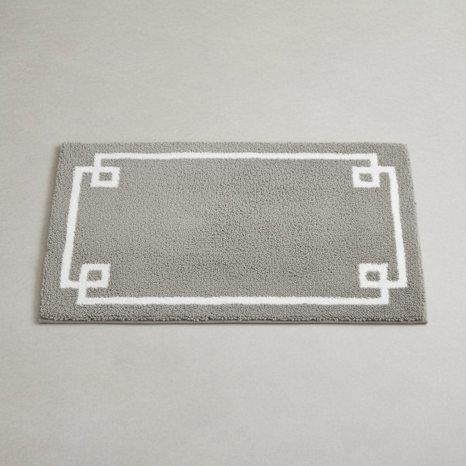 Gray bath mat with white border in front of a white bathtub in a bathroom setting.